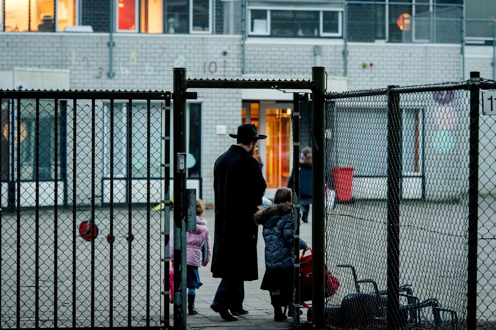 Orthodox-Joodse vader brengt kinderen naar school achter een hek